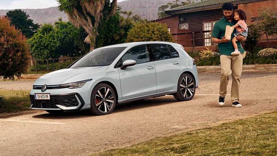 Volkswagen Golf GTE v bílé barvě zaparkovaný na silnici u příjezdové cesty. Vedle vozu stojí muž, který na ruce drží svou dceru.