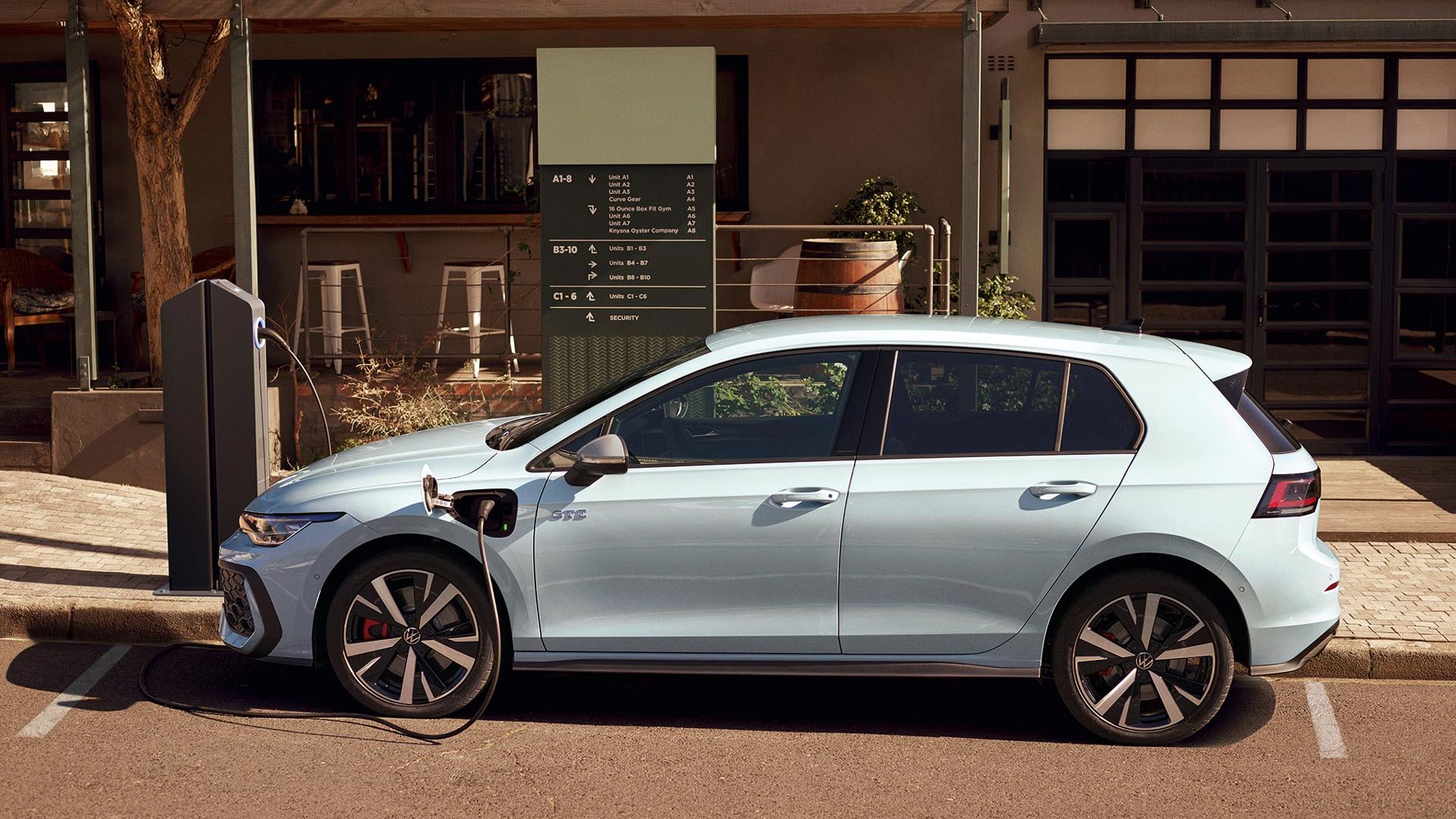 Volkswagen Golf GTE v bílé barvě zaparkovaný před restaurací je připojený k nabíjecí stanici.