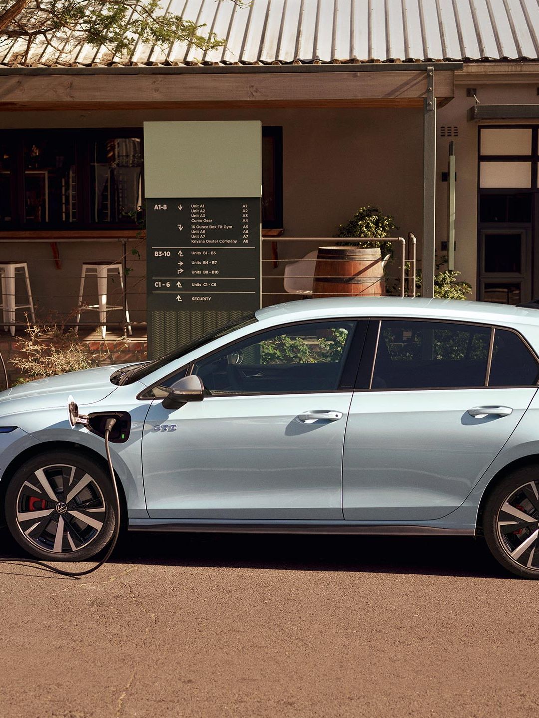 Volkswagen Golf GTE v bílé barvě zaparkovaný před restaurací je připojený k nabíjecí stanici.