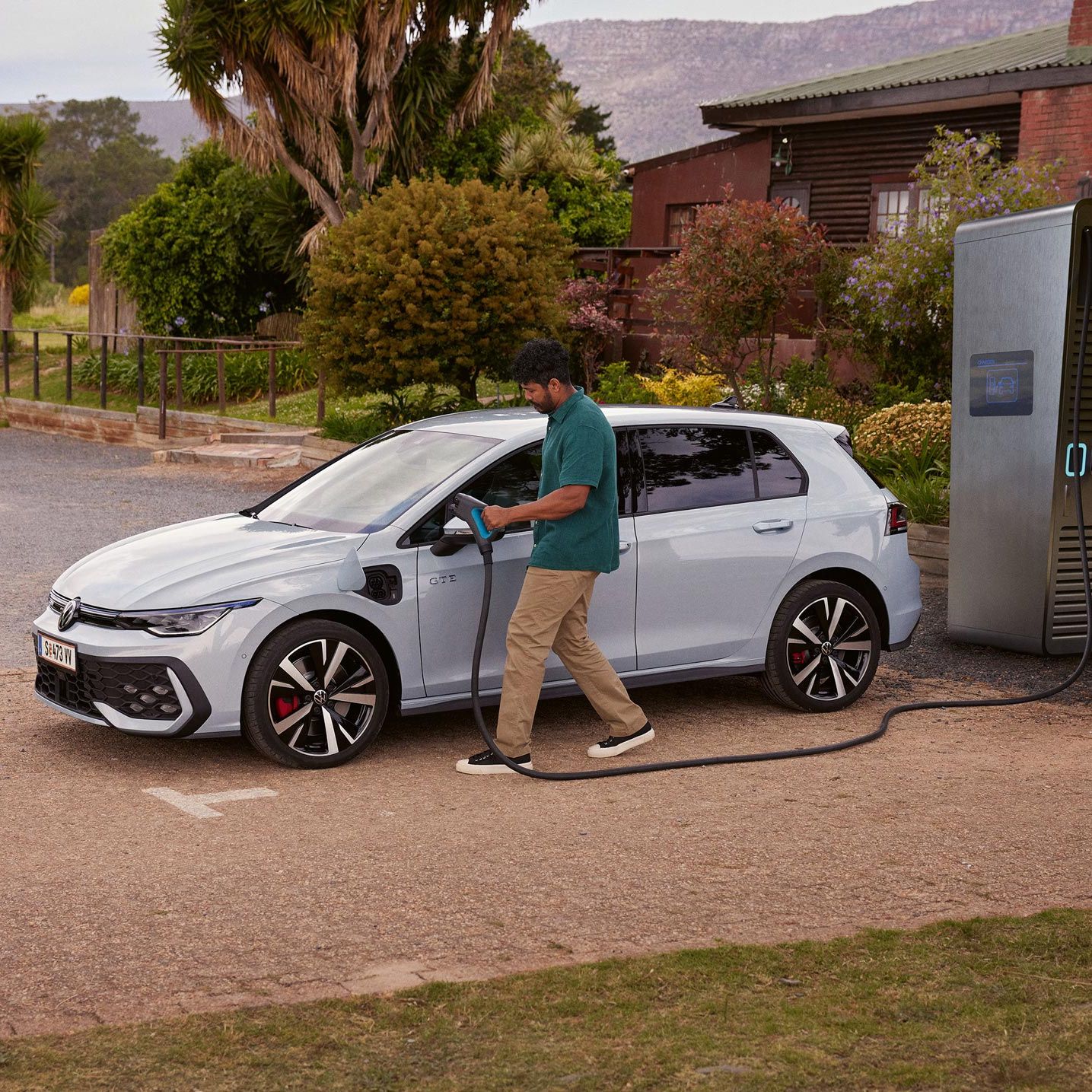 Muž připojuje nabíjecí kabel od nabíjecí stanice se stejnosměrným proudem k nabíjecímu portu vozu Volkswagen Golf GTE v bílé barvě.