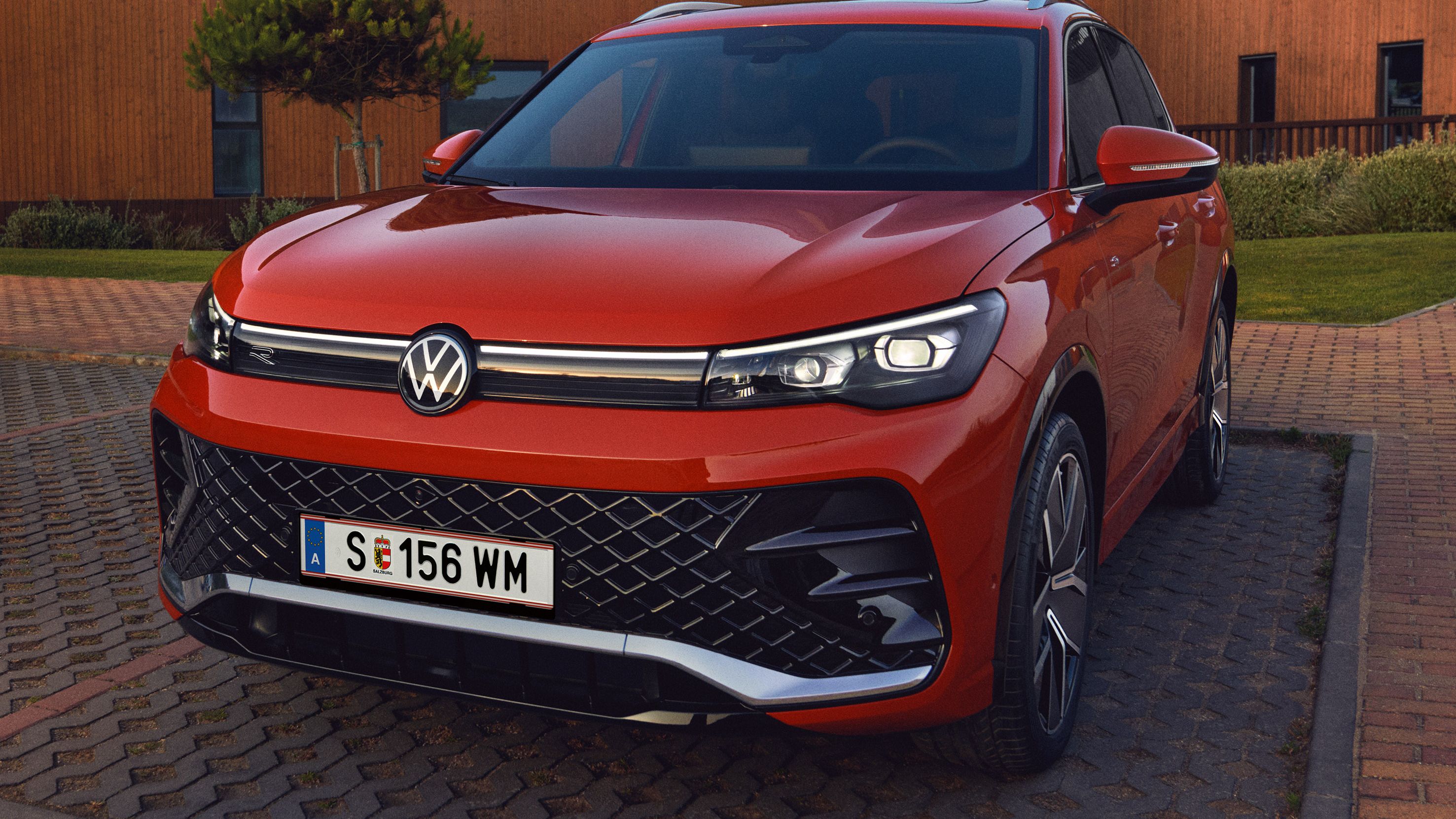 Detailní pohled na čelní světelnou signaturu modelu Volkswagen Tiguan v červené barvě stojícího na parkovišti.